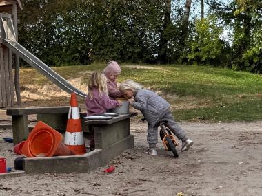 Tre børn er optaget af at fremtrylle lækker mad i sandkassen.